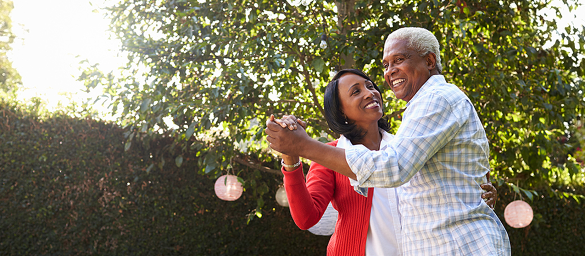 An older adult couple dances in their backyard.
