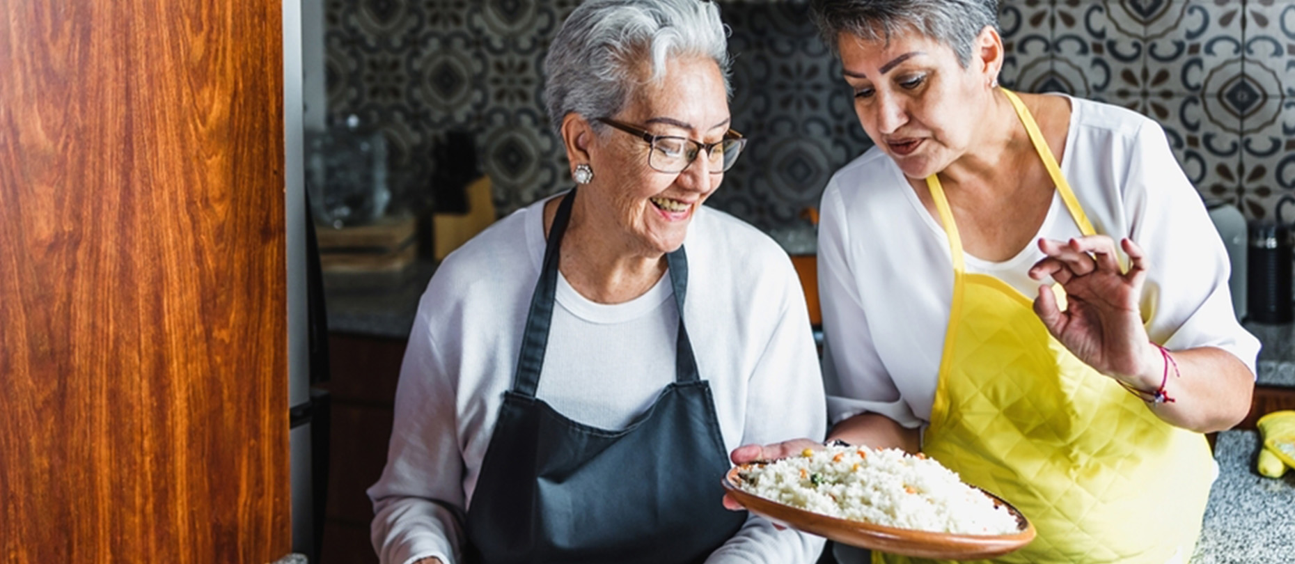 A mother and her adult daughter cook in the kitchen.