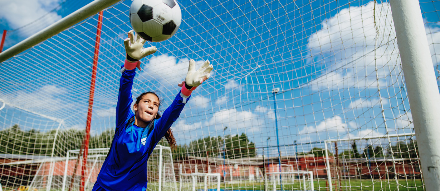 A soccer goalie stretches to block a shot on goal.