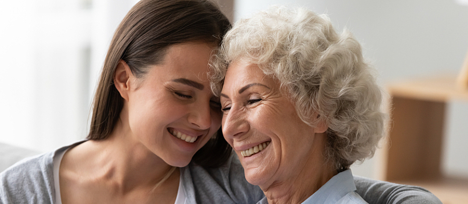 A young woman and an older woman smile with their heads close together.