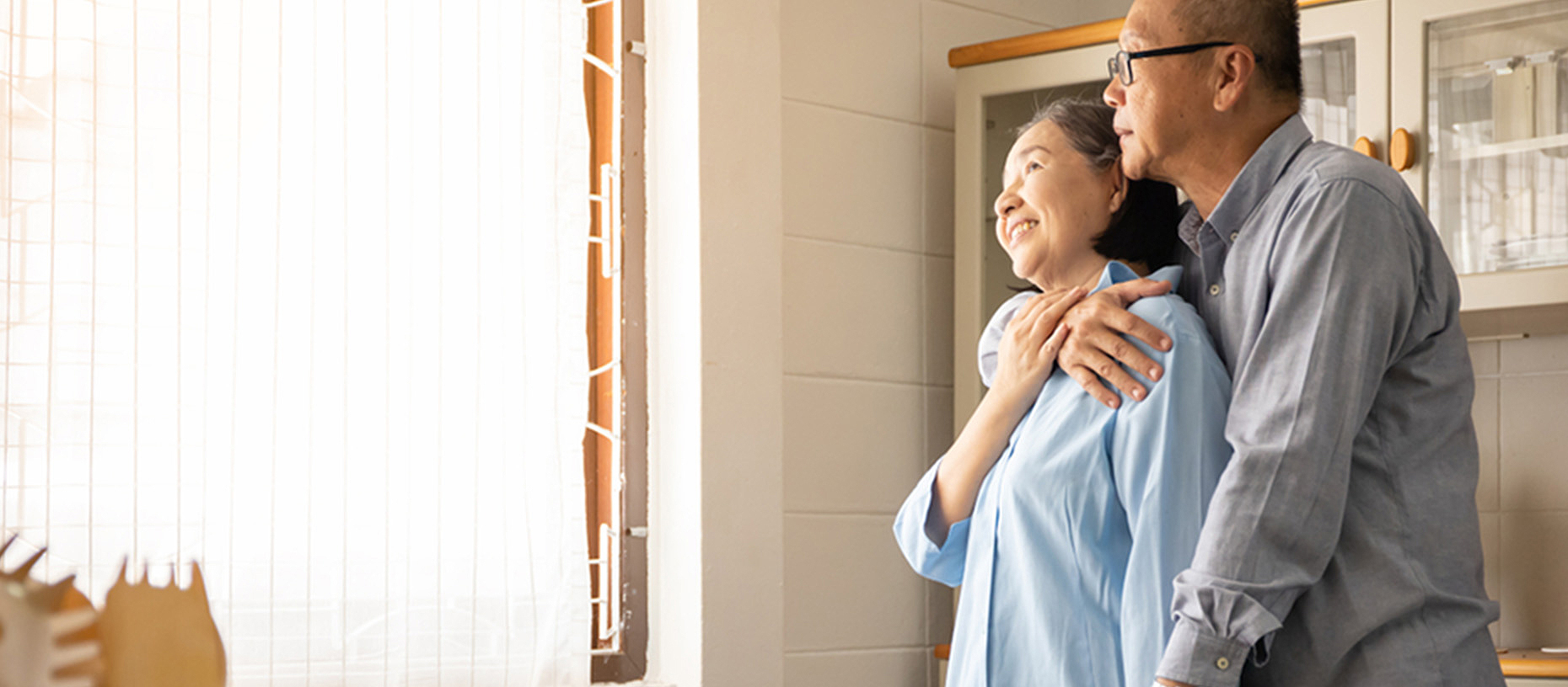 An older couple embraces in a kitchen.