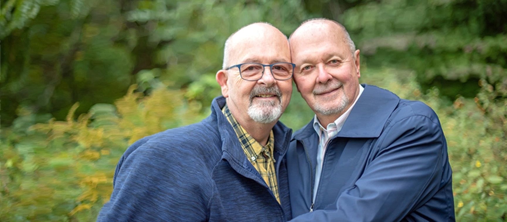 An older male couple smiles with their heads together.
