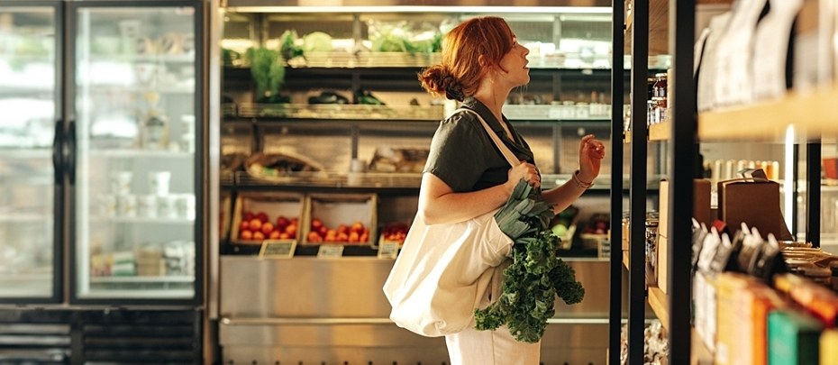 Person holds a reusable bag filled with leafy greens as they shop at the grocery store