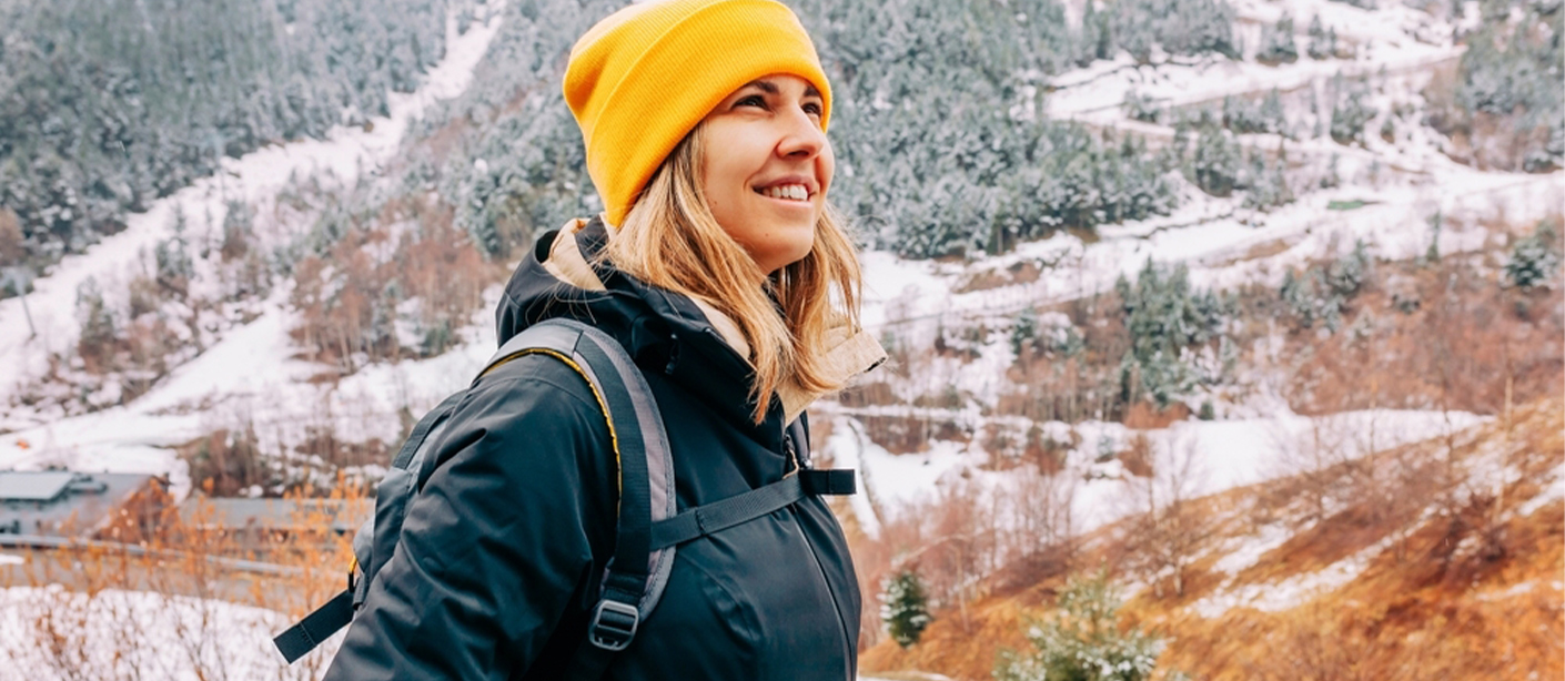 A person wearing a coat, hat and backpack hikes in snowy mountains.