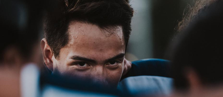 A man in a soccer uniform peeks up from within a team huddle.