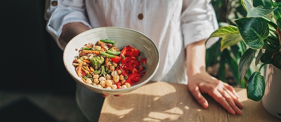 A person holds out a bowl filled with vegetables and legumes.
