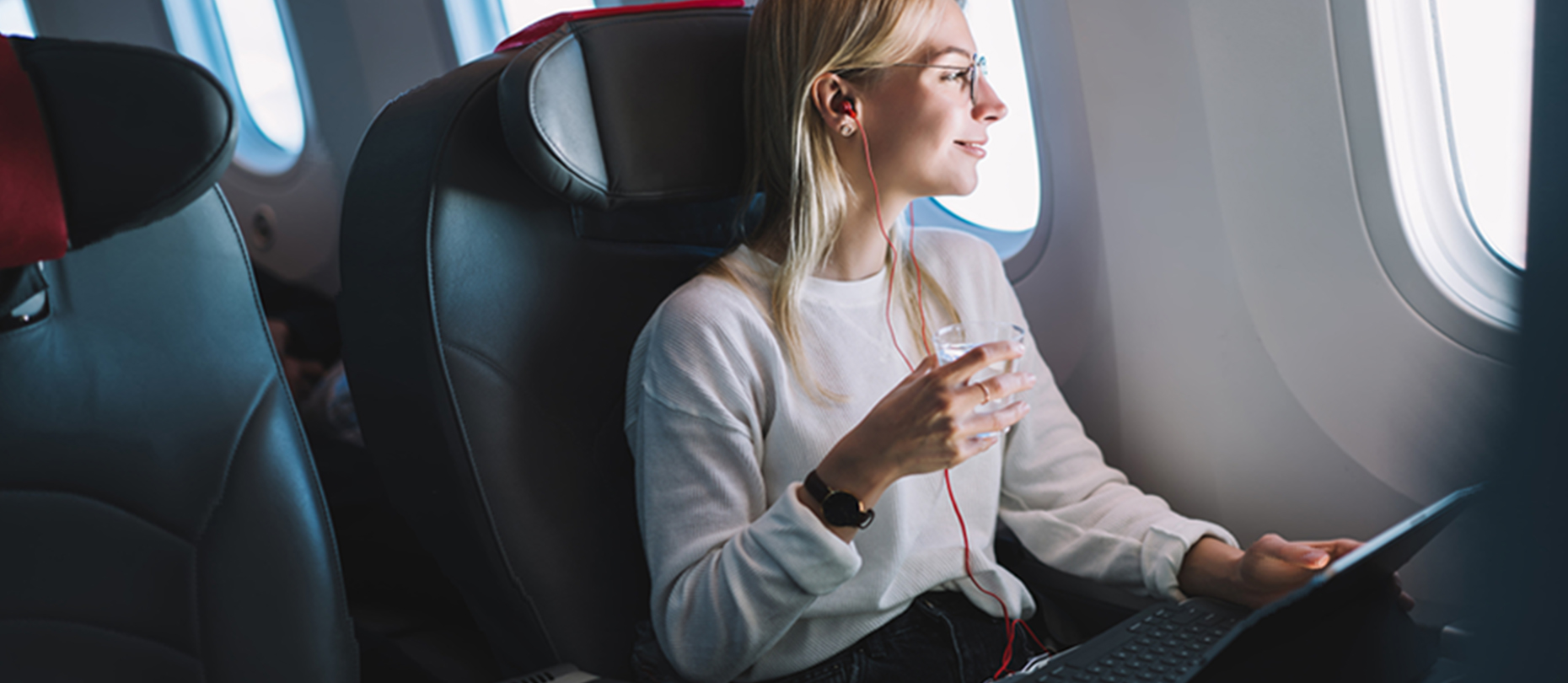 A woman drinks a glass of water on an airplane.