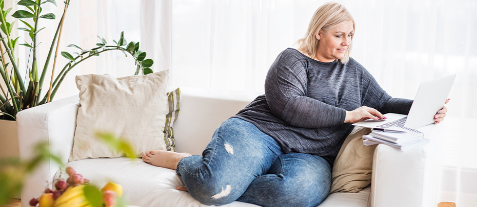 A woman reads on a laptop computer while sitting on her couch.