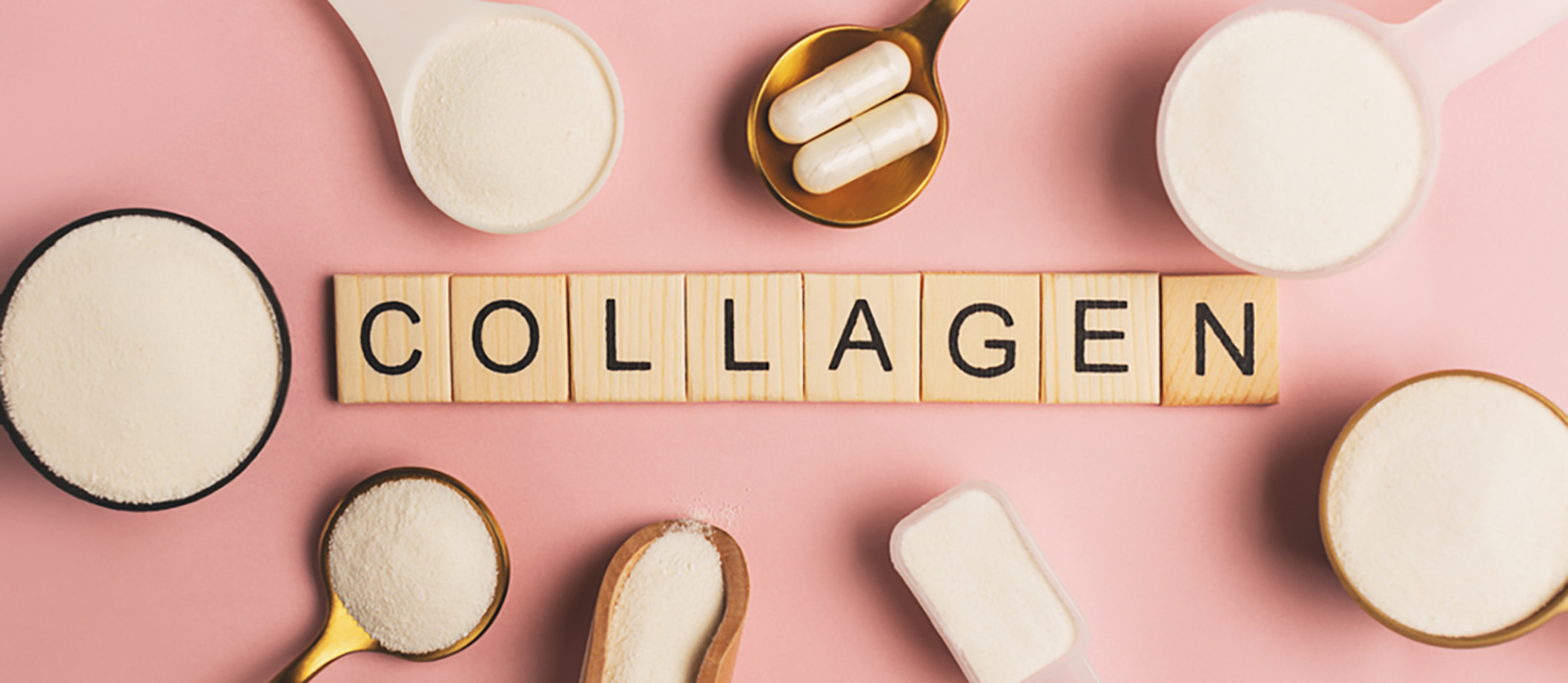 Spoons filled with powders and capsules surround the word collagen in wooden letters.