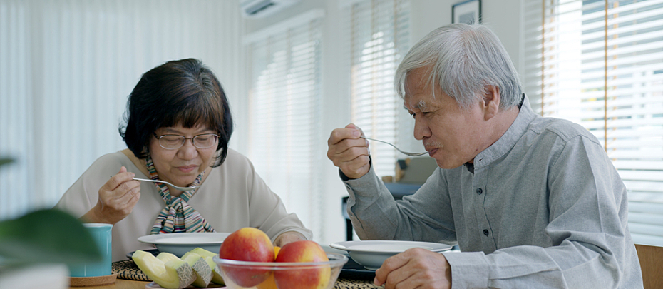 Older couple sits at a table, sipping soup.