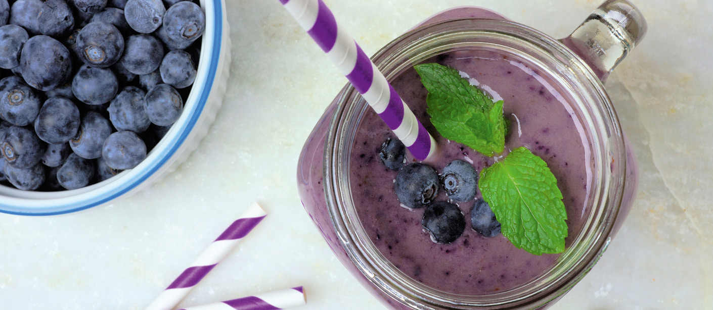 A bowl of blueberries and a blueberry smoothie.  