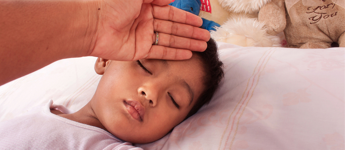 A person holds the back of their hand to a sleeping child's forehead.