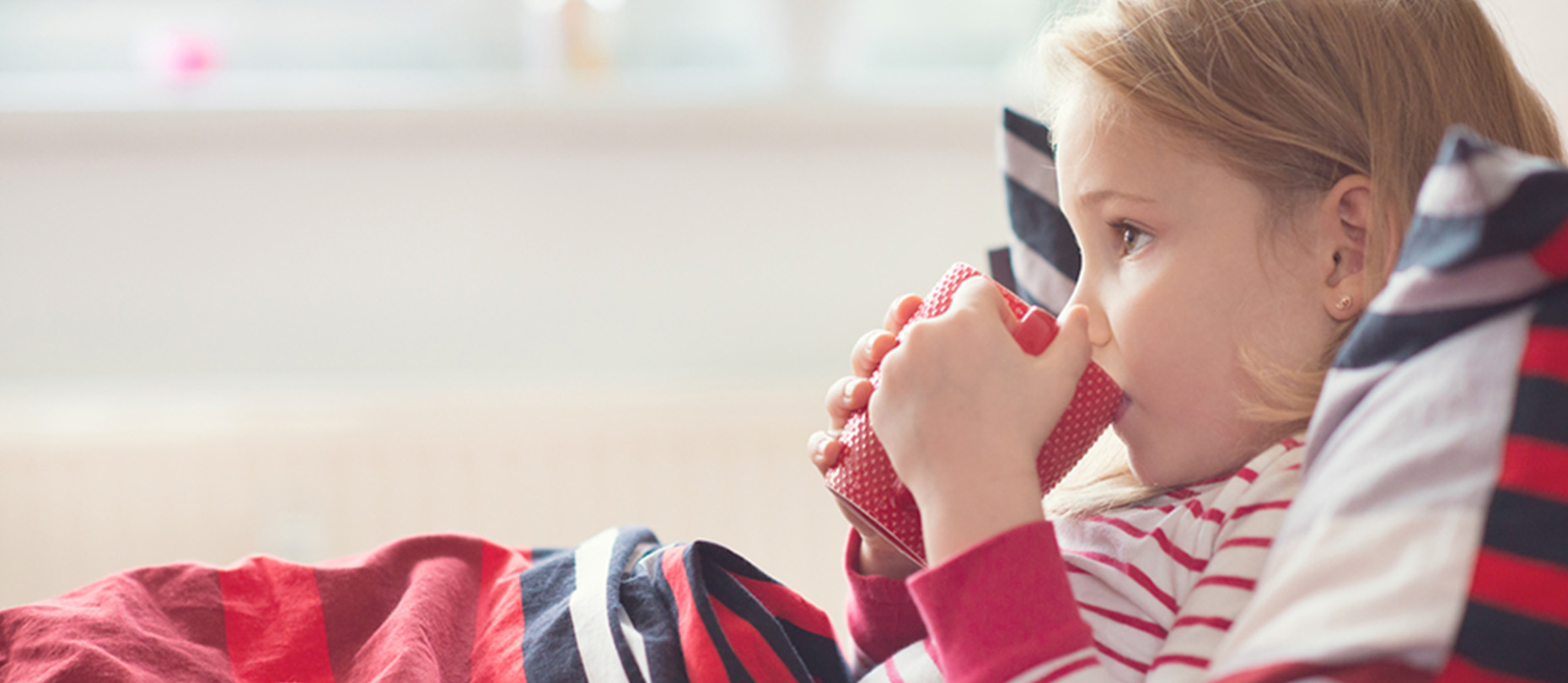 A child lies in bed drinking out of a red cup.