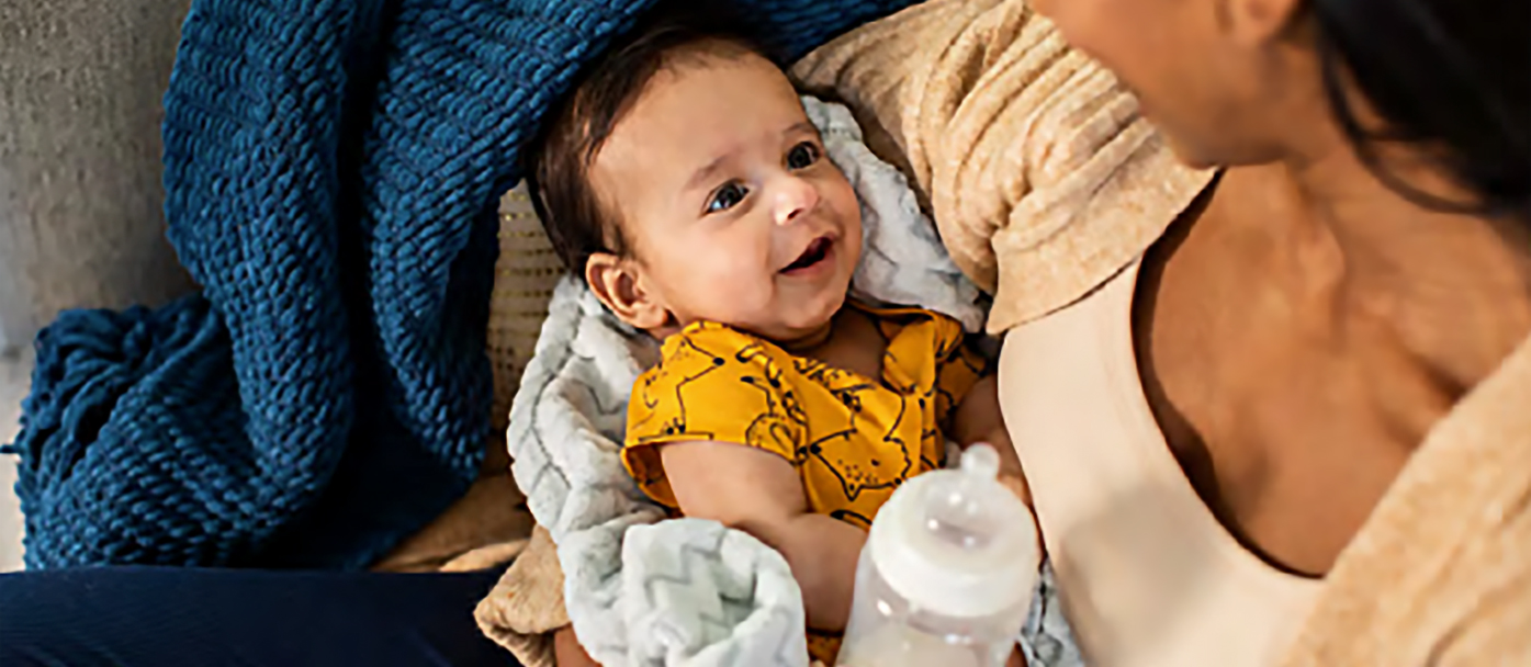 A woman looks down at a smiling baby, while holding a bottle.