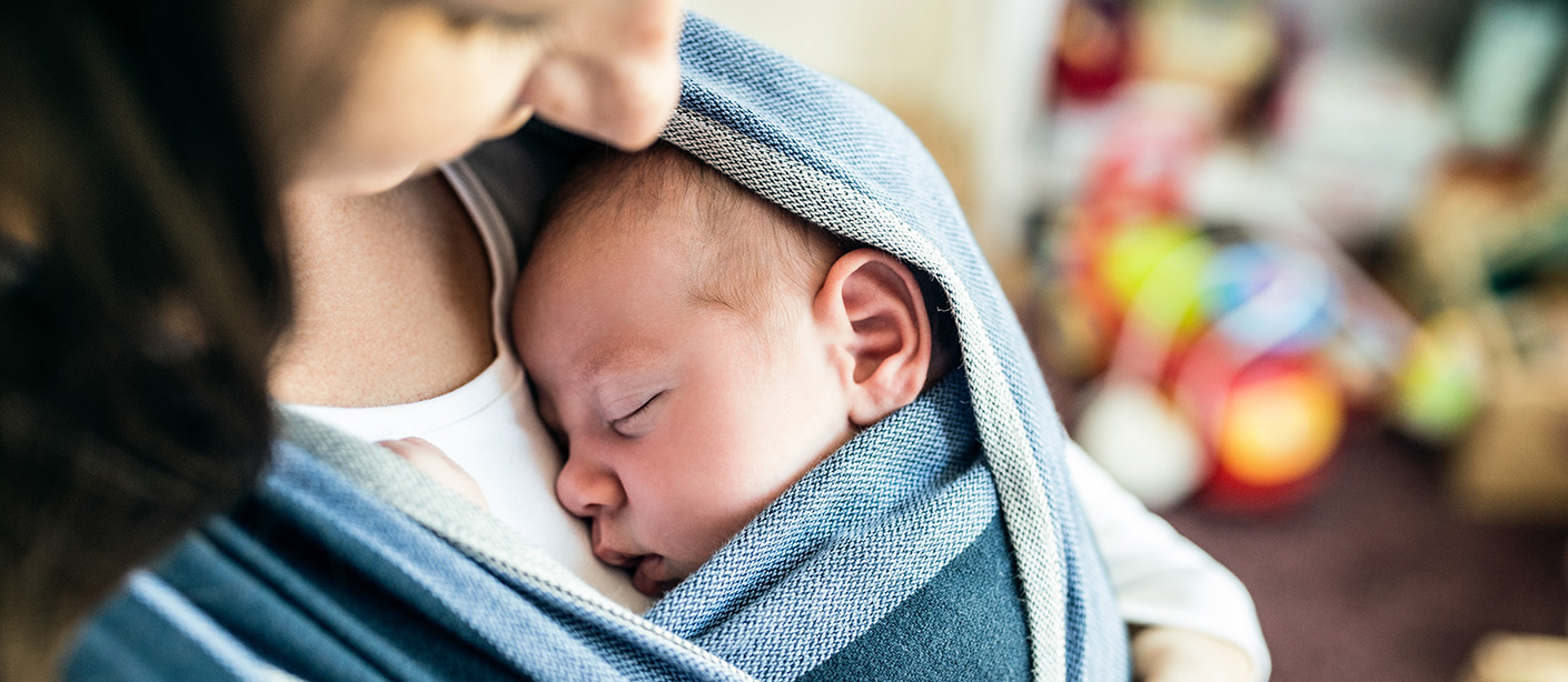 Mom holding a sleeping baby wrapped in a blue cloth baby carrier