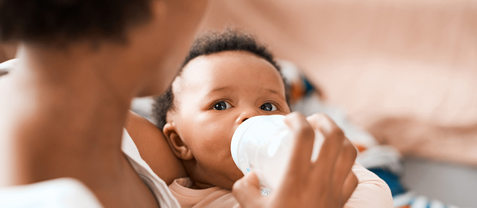A mother cradling a baby while feeding a bottle