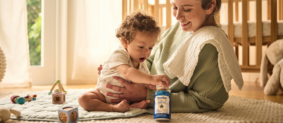 Mom playing with her baby on the floor while baby grabs Similac bottle