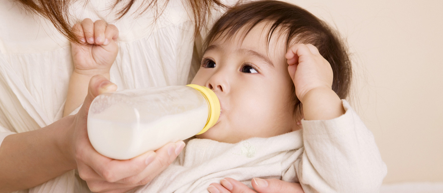 A person holds a baby in their arms and feeds them a bottle of formula.