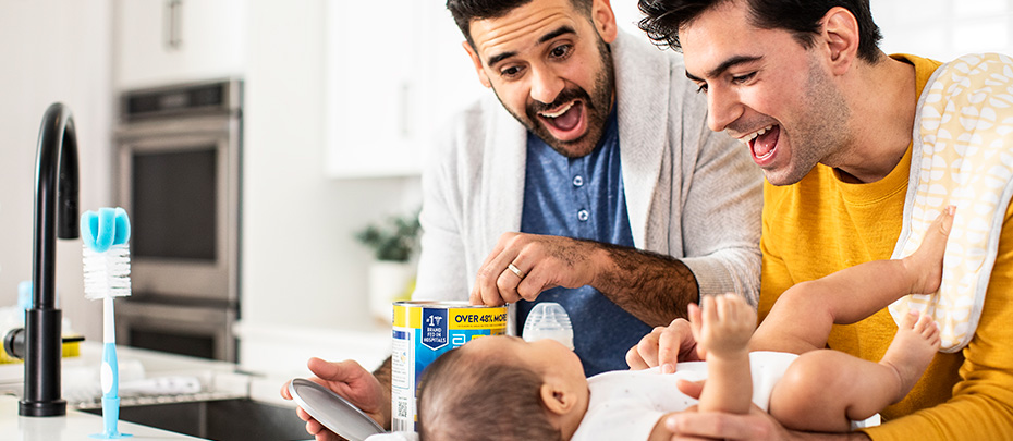 Parents smile at baby as they make a baby bottle of formula.