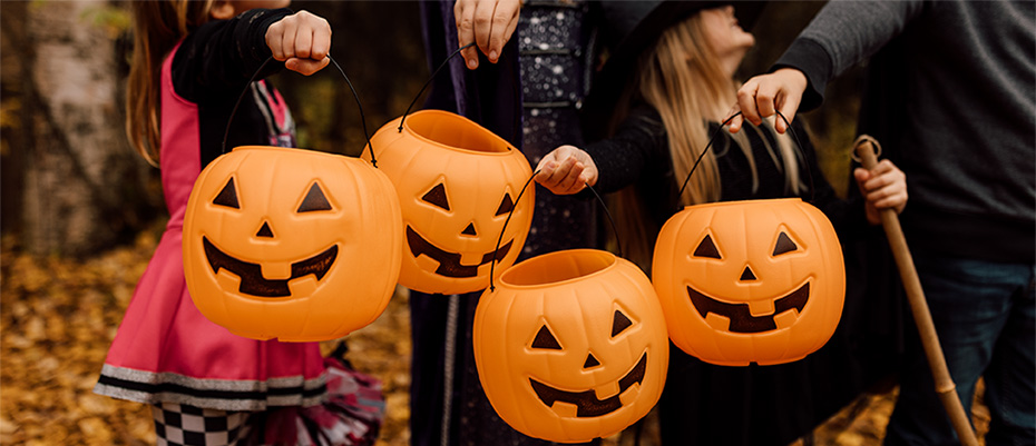 Four kids in Halloween costumes stand outside with their pumpkin trick-or-treat buckets